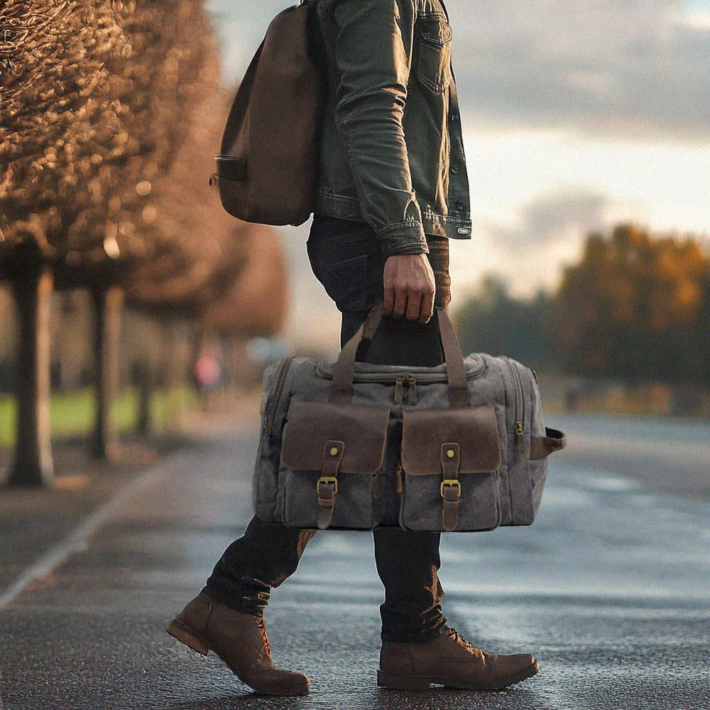 Person walking with a stylish grey weekend duffle bag in a scenic outdoor setting.