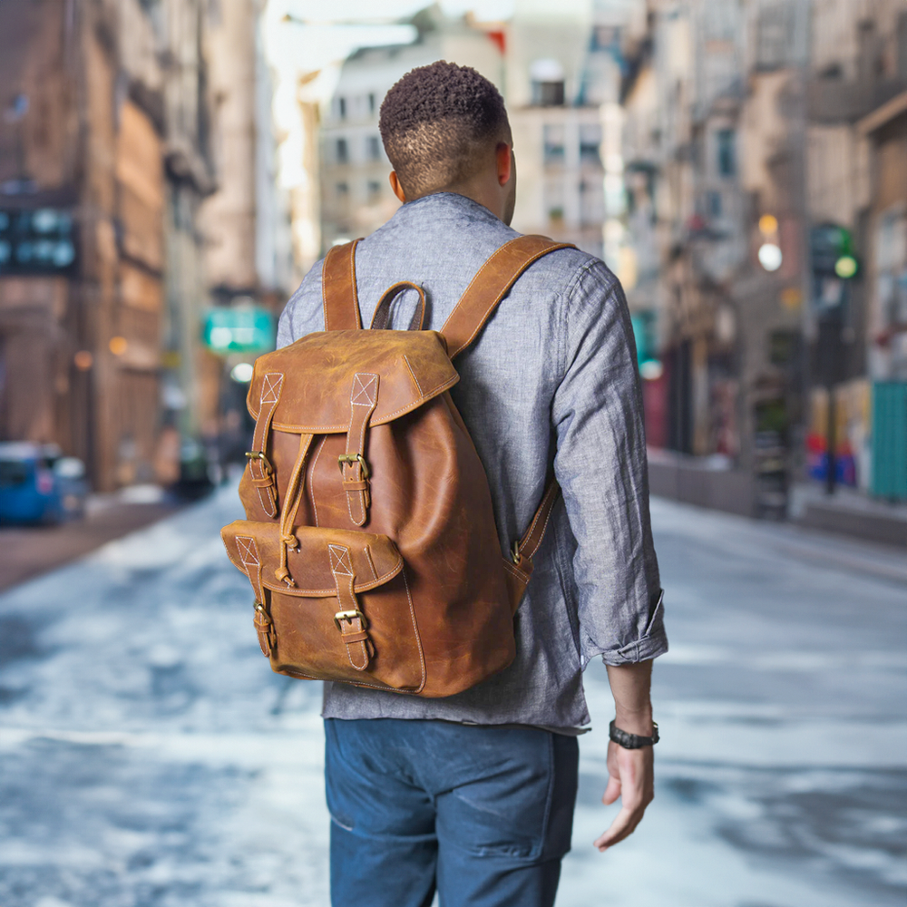 Stylish man walking in the city with a brown leather knapsack, showcasing urban fashion and functionality.