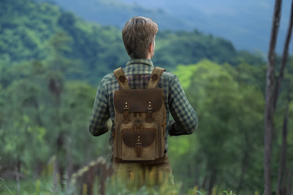 Man wearing a vintage leather camera backpack while hiking in a lush green landscape.
