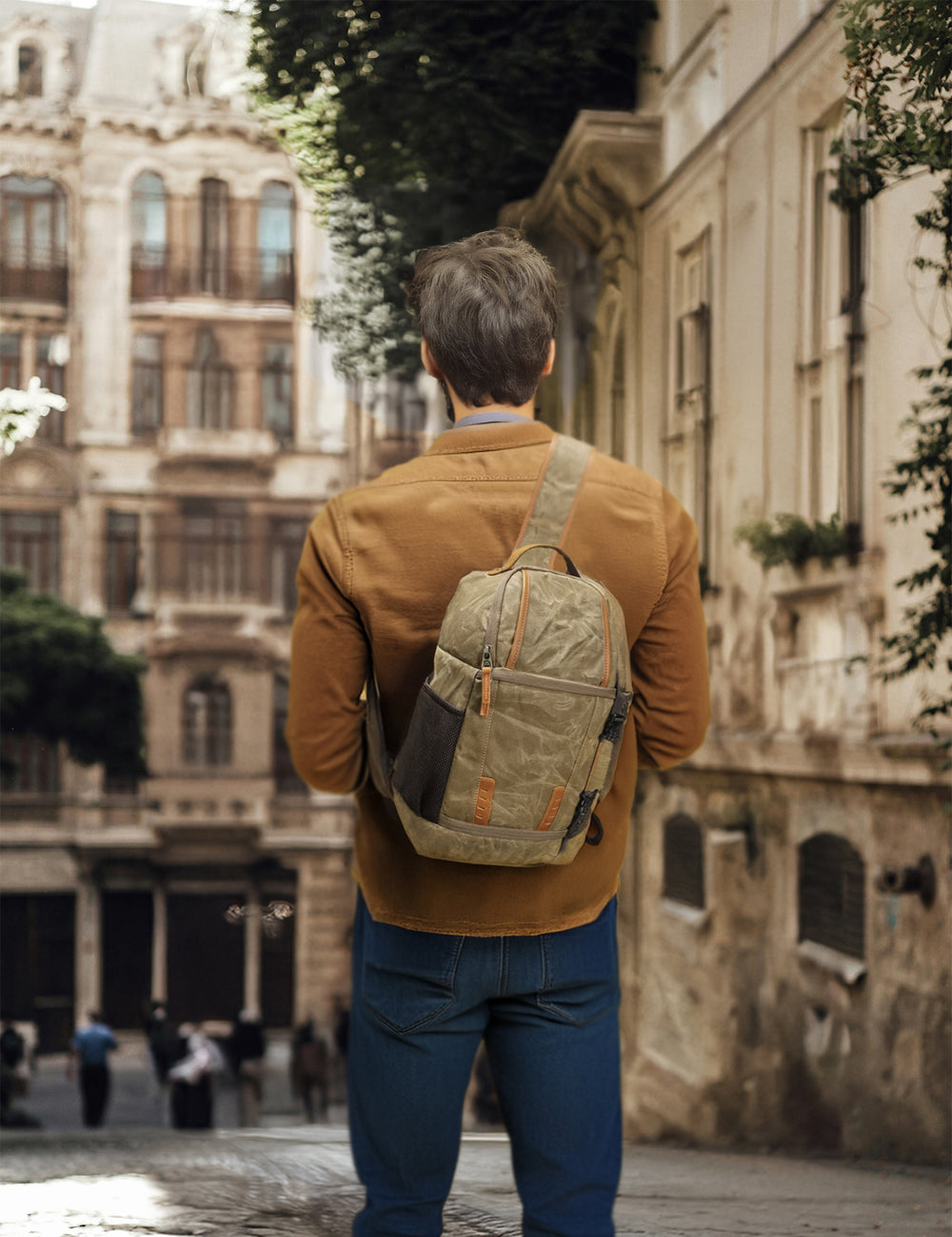 Stylish man wearing a canvas camera sling bag, walking through a historic street, perfect for adventures.