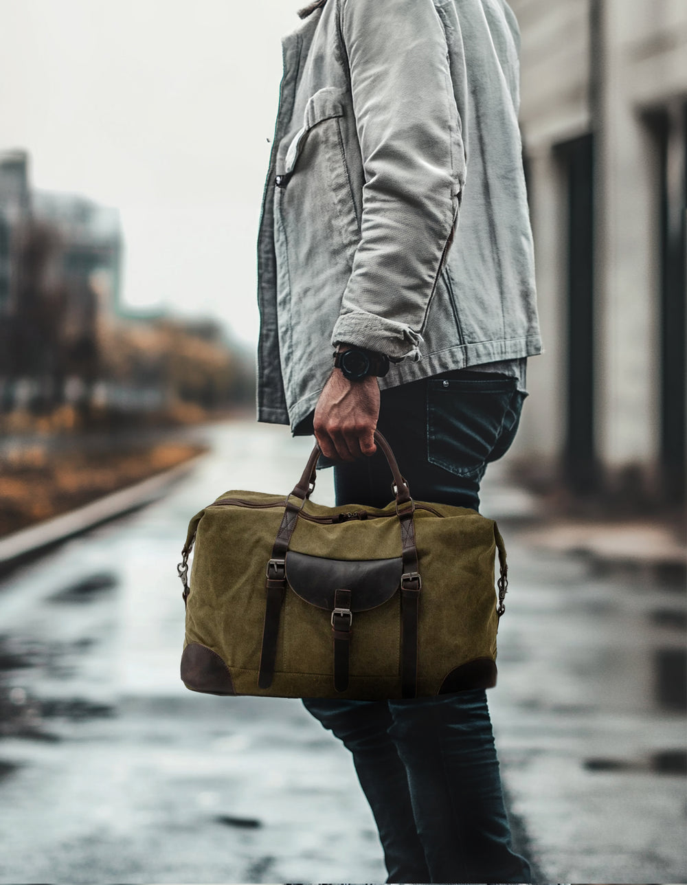 Model carrying a stylish green canvas overnight bag while walking along a rainy street.