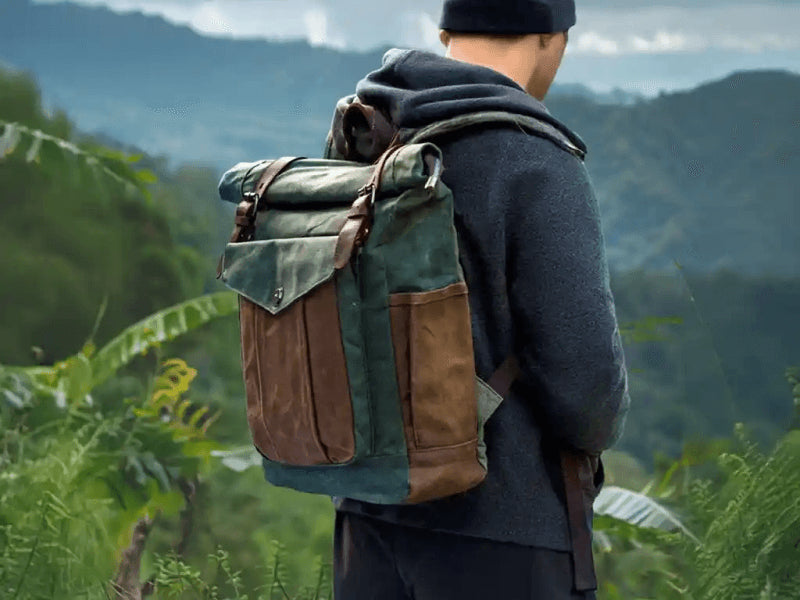 Man wearing a stylish outdoor backpack while surrounded by lush greenery and mountains in the background.