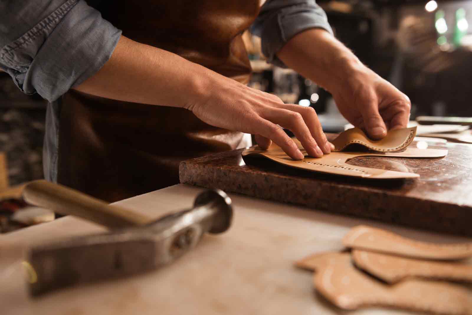 Skilled artisan crafting leather pieces on a workbench with tools and materials for shoemaking.