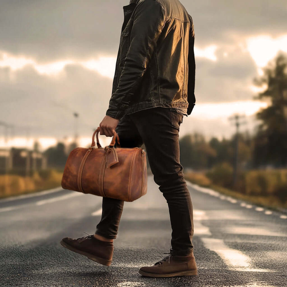 Man walking on a road holding a stylish leather duffle bag, perfect for travel and adventure.