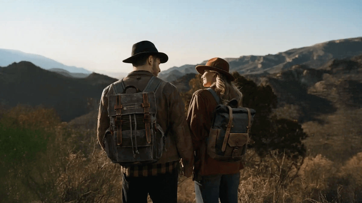Couple standing in a mountainous landscape wearing stylish backpacks, enjoying nature together.