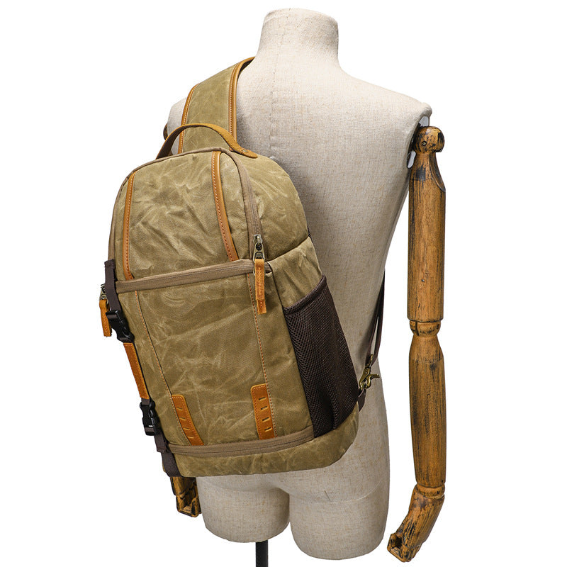 Canvas camera sling bag in olive green, displayed on a mannequin against a neutral background.