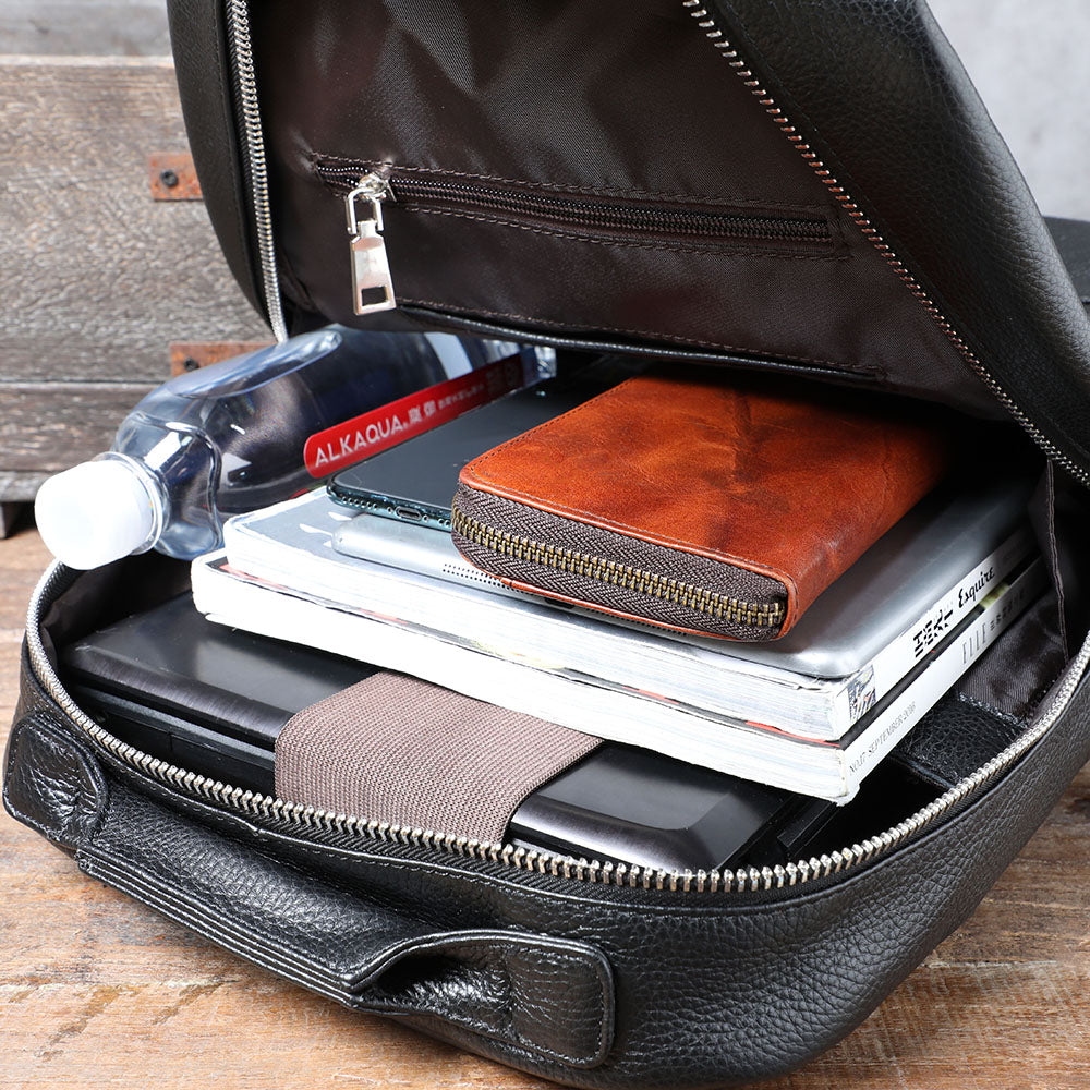 Inside view of a black leather bookbag filled with notebooks, a wallet, and a water bottle, showcasing its spacious design.