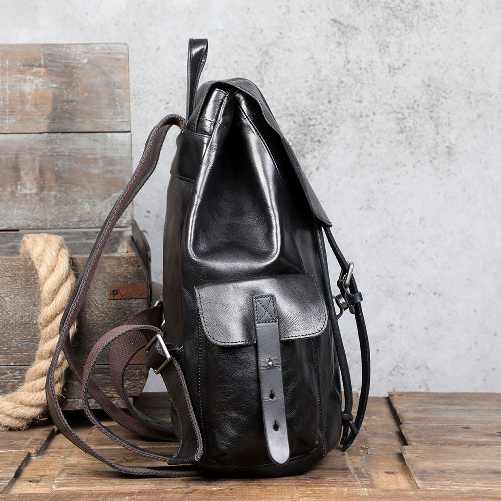 Small black leather backpack with adjustable straps, stylish design, and front pocket on wooden surface.