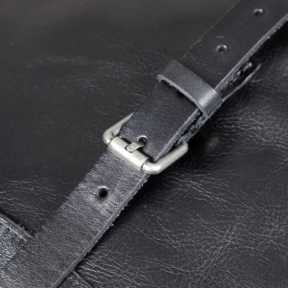 Close-up of a silver buckle and black leather strap on a small black leather backpack.