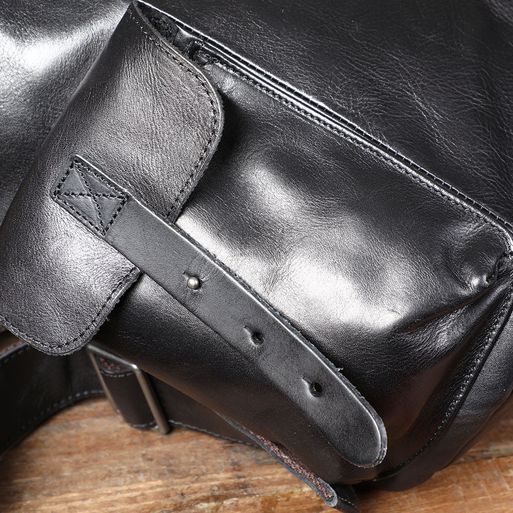 Small black leather backpack detail featuring sleek finish and buckle strap, perfect for stylish outings.