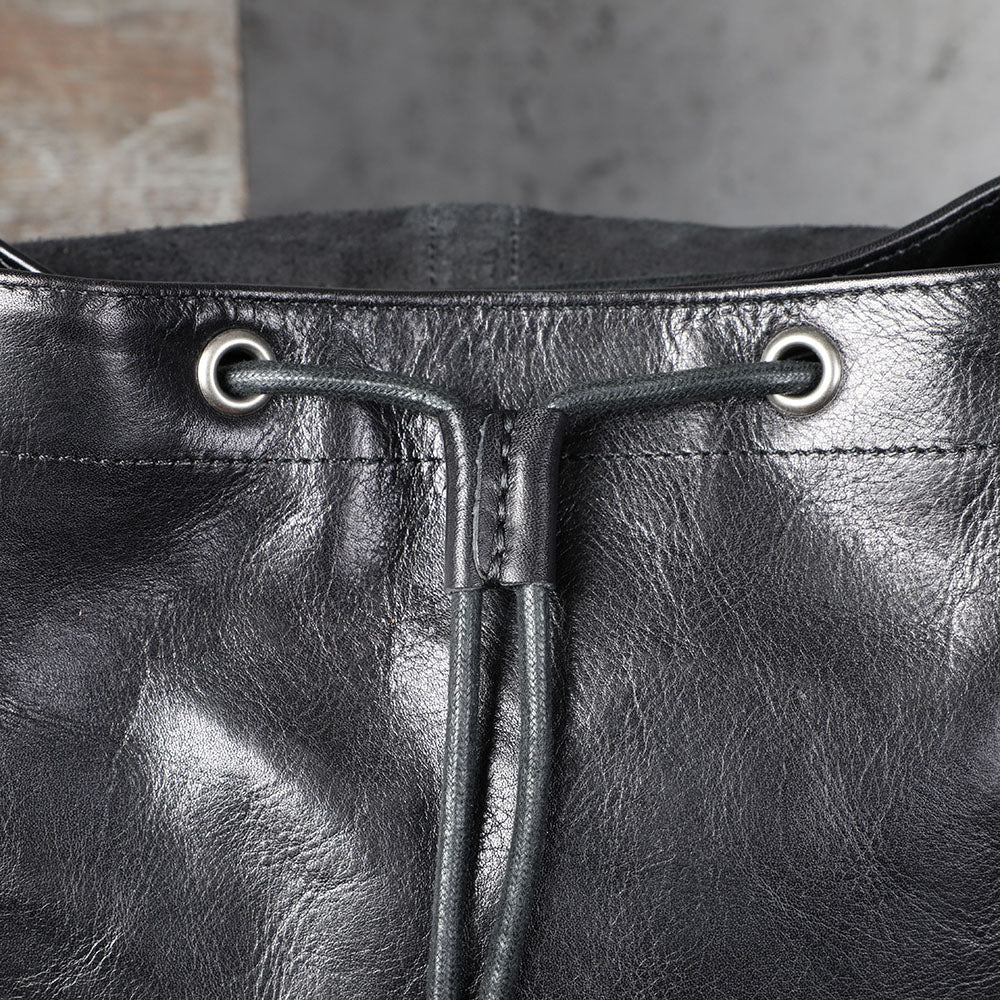 Close-up of the top of a small black leather backpack with drawstring closure and metal eyelets.