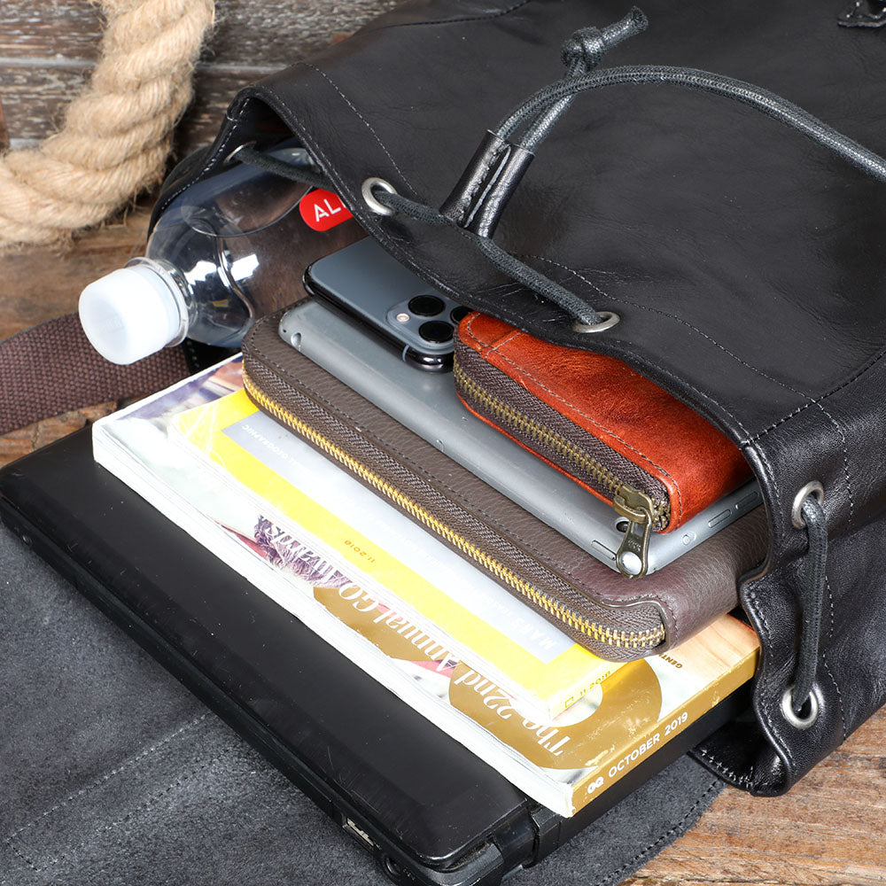 Inside a small black leather backpack, showcasing a laptop, phone, wallets, and a water bottle.