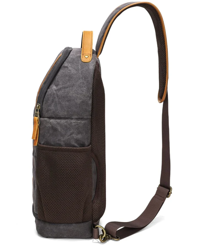 Canvas camera sling bag with brown leather accents, mesh side pocket, ideal for travel and outdoor adventures.