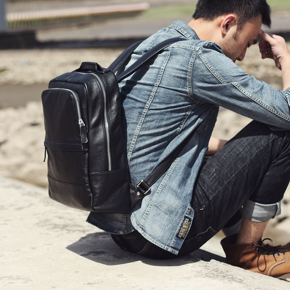 Stylish black leather bookbag resting on a man in a denim shirt, showcasing the sleek design and practicality.