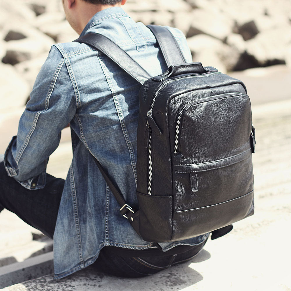 Man wearing a black leather bookbag against a rocky background, showcasing style and durability.