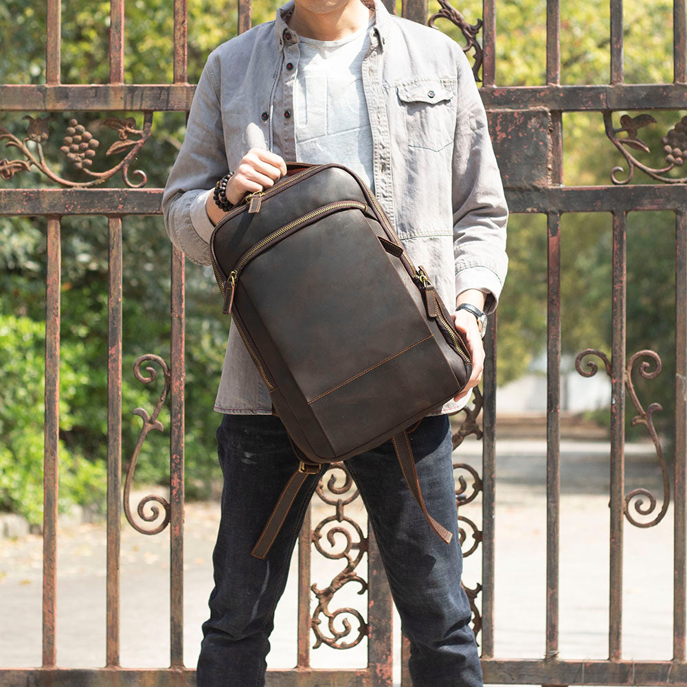 Leather laptop rucksack named Loch Ness, stylishly held by a person in front of an ornate gate outdoors.