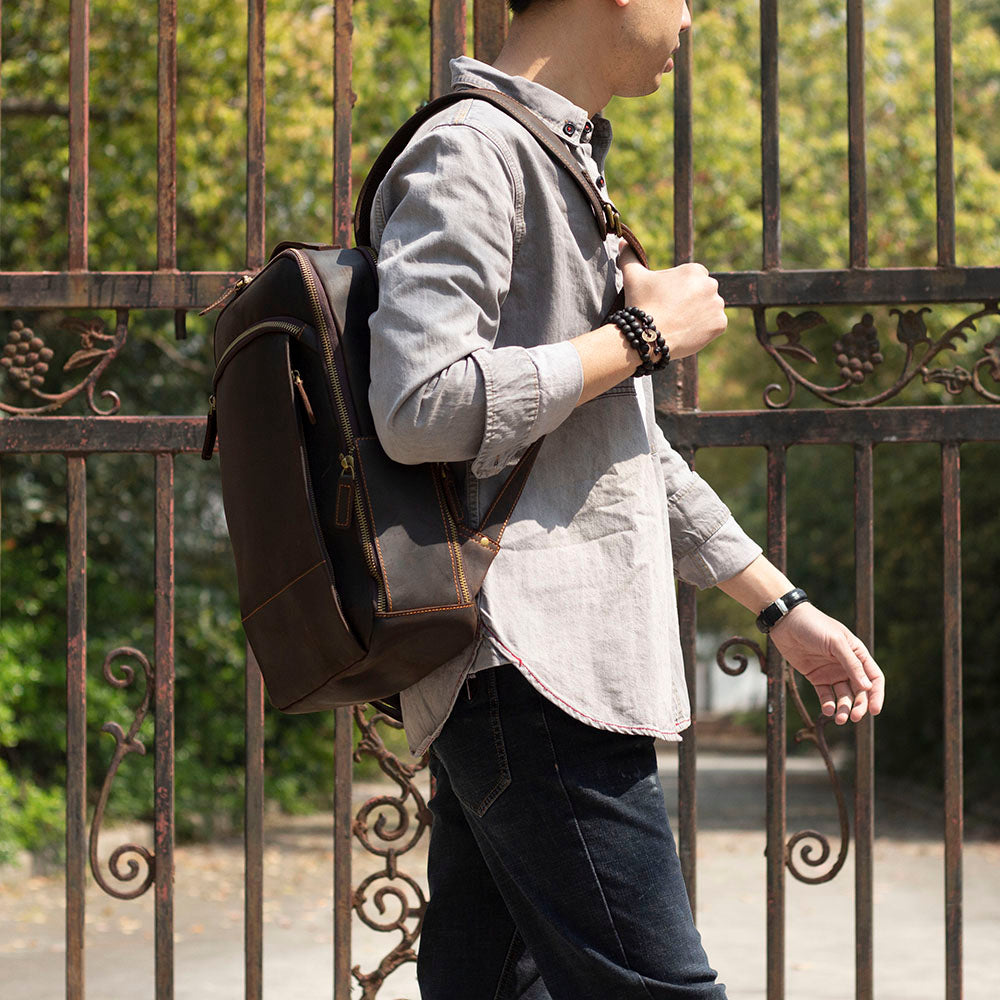 Man walking with a stylish leather laptop rucksack against a decorative iron gate.