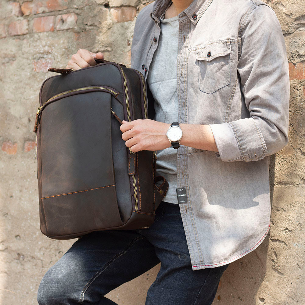 Man holding a stylish Leather Laptop Rucksack, perfect for daily use, standing against a rustic brick wall.