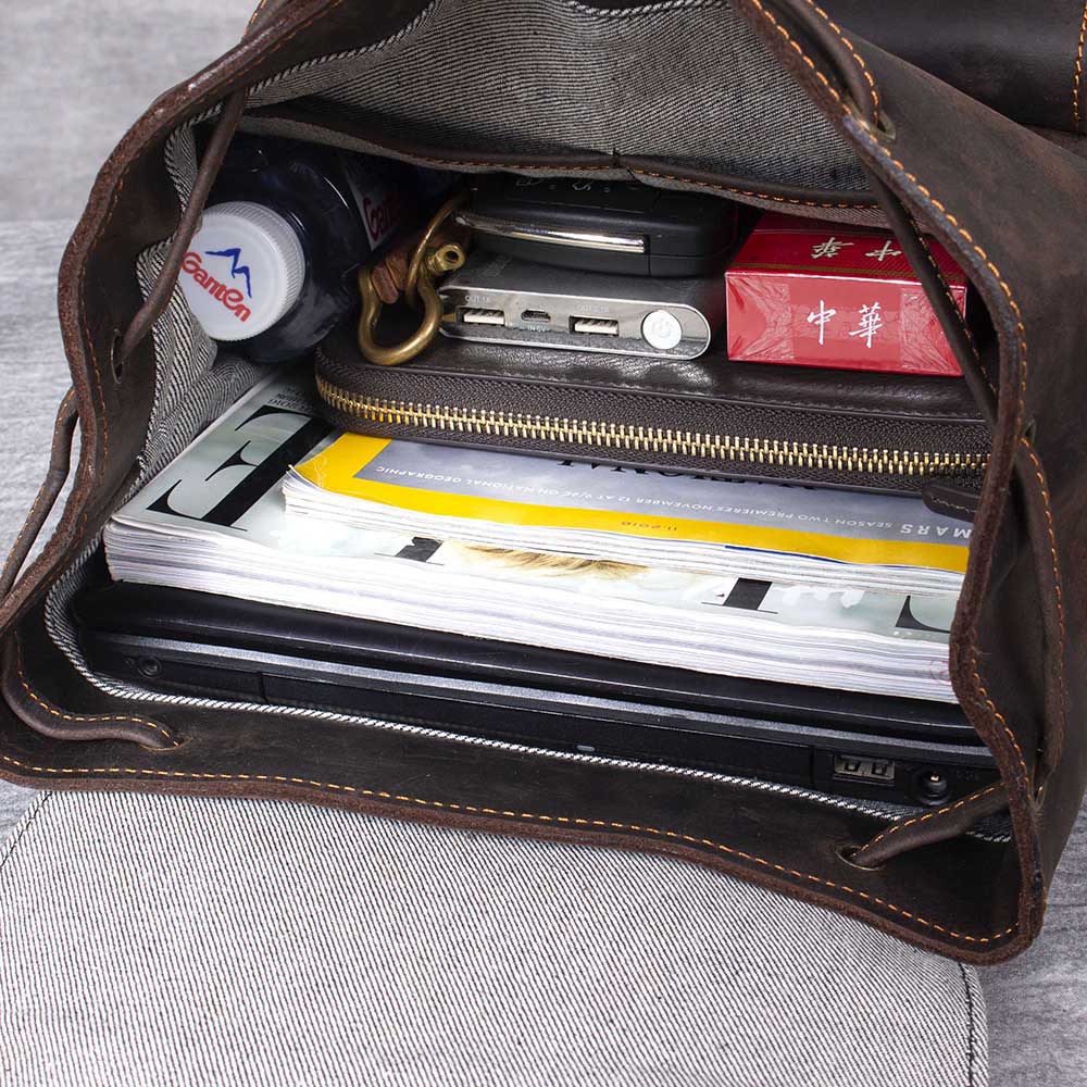 Interior view of a leather drawstring backpack, showcasing organized items like books, a laptop, and personal essentials.