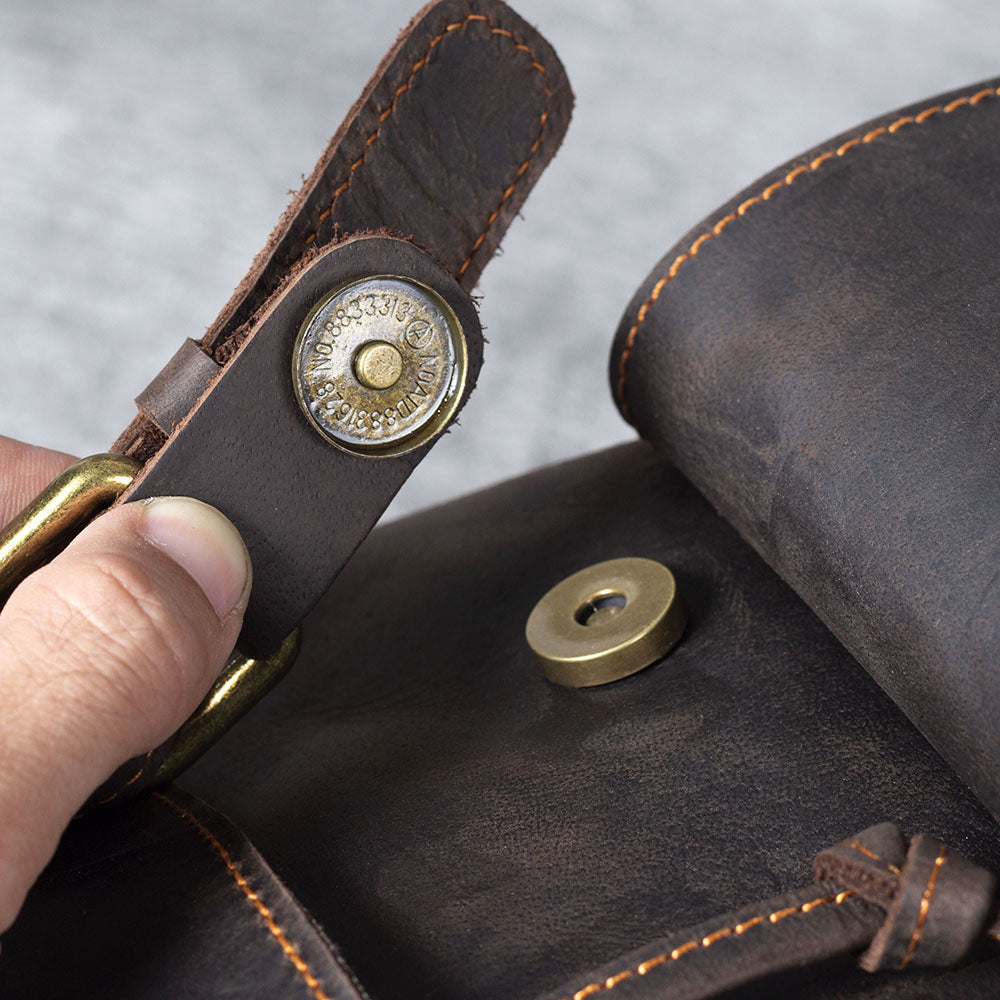 Close-up of a leather drawstring backpack's brass clasp, showcasing its quality stitching and craftsmanship.
