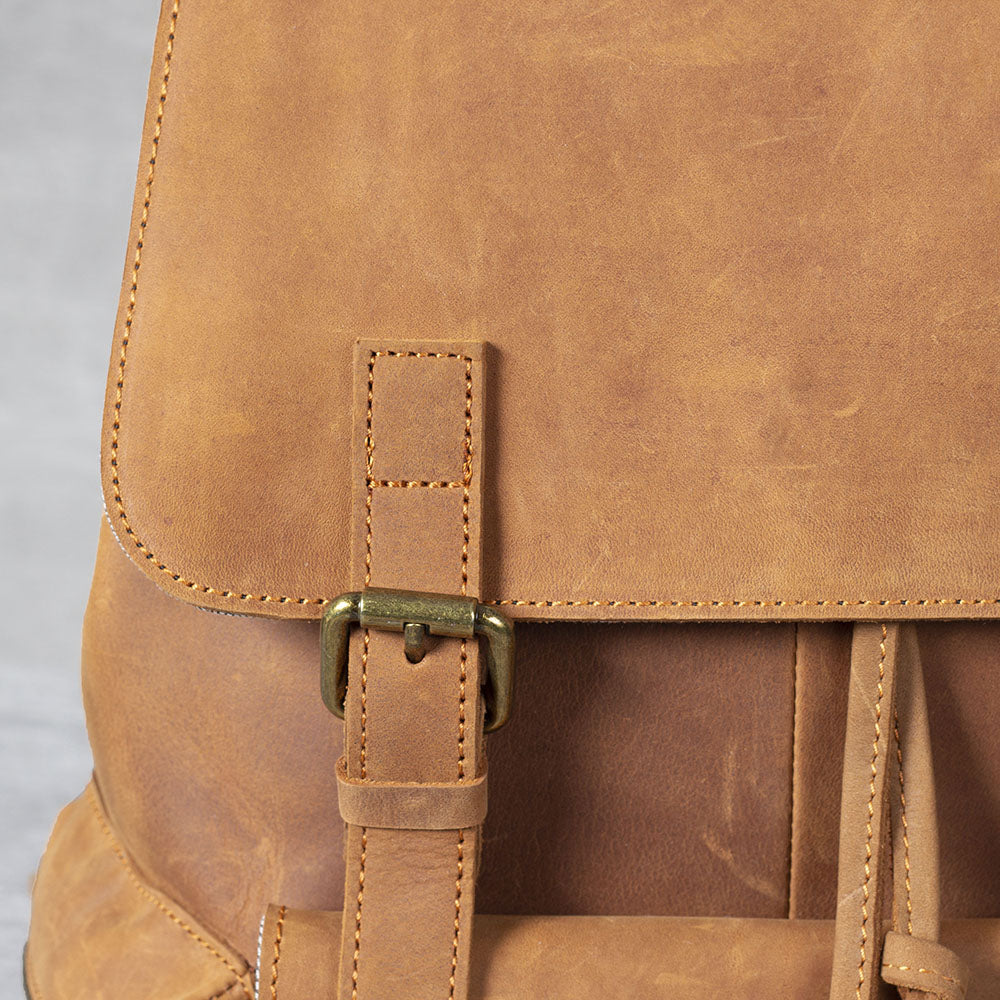 Close-up of a leather drawstring backpack with brass buckle detailing, showcasing its tan finish and quality craftsmanship.