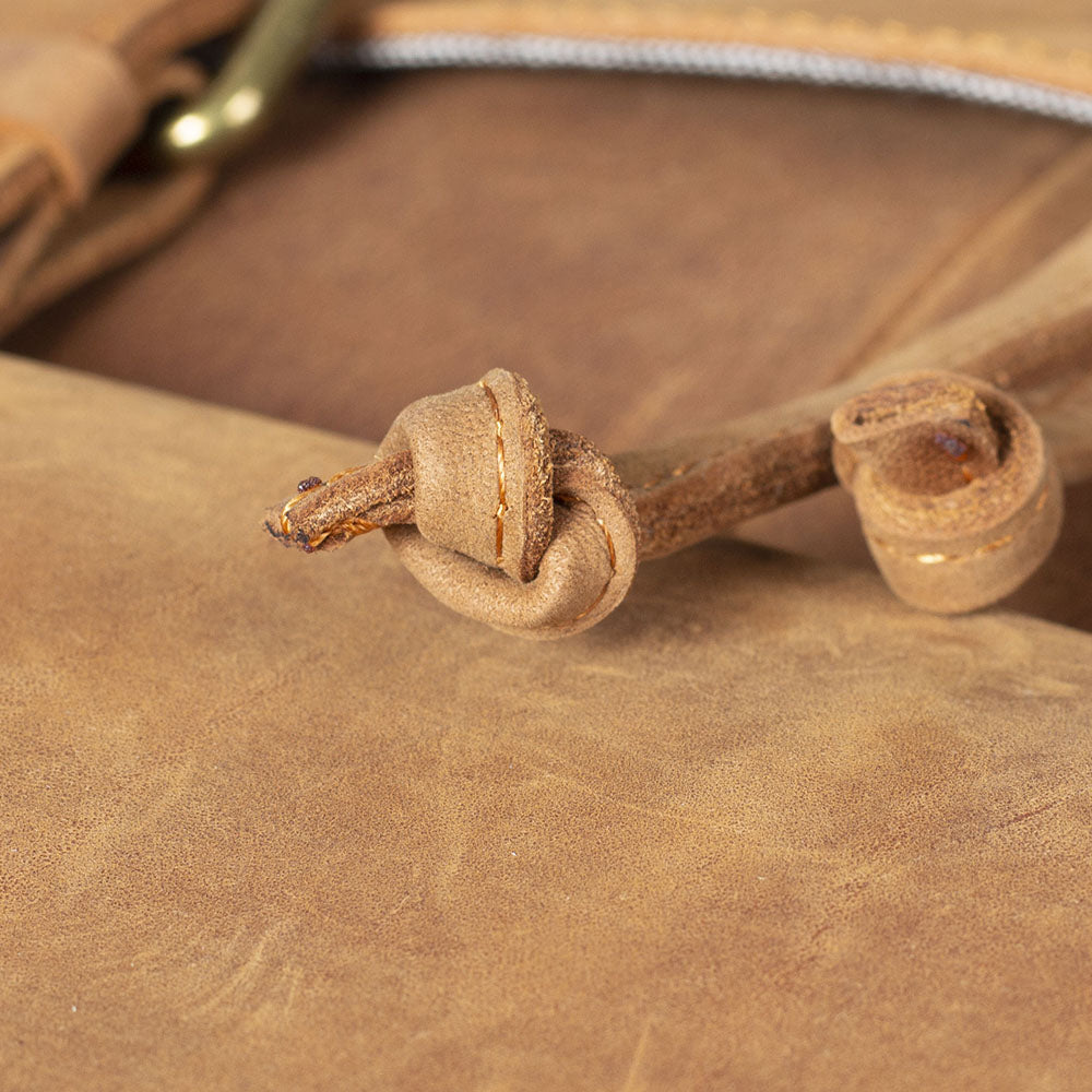 Close-up of a leather drawstring knot on a tan leather backpack, showcasing quality craftsmanship and design.