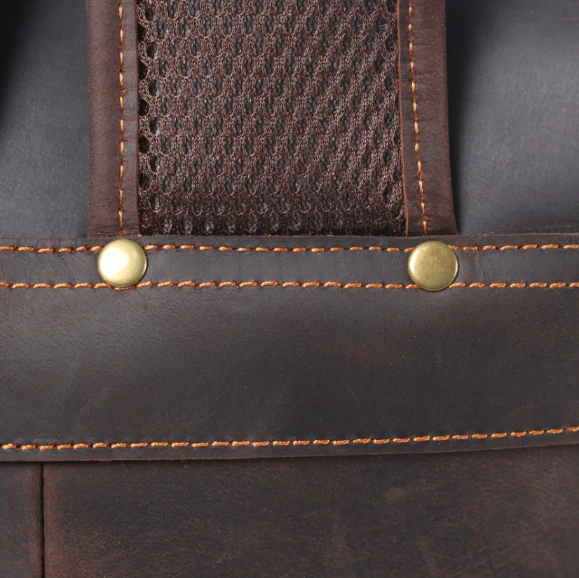 Close-up of brown leather drawstring backpack strap with gold rivets and stitching details.