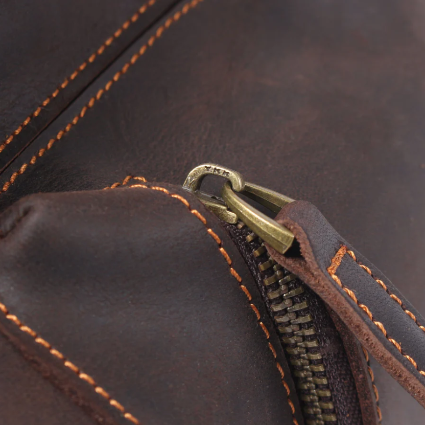 Close-up of a leather backpack zipper showcasing detailed stitching and a smooth metal pull.