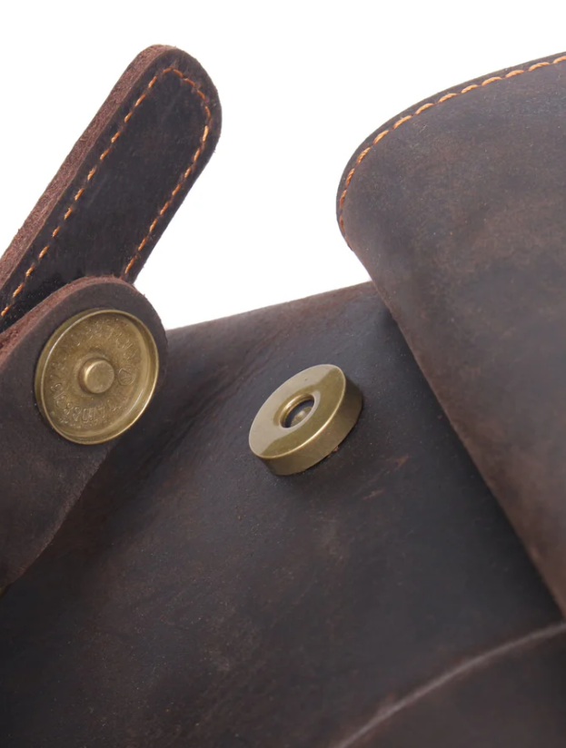 Close-up of a leather drawstring backpack with brass hardware and stitching detail.