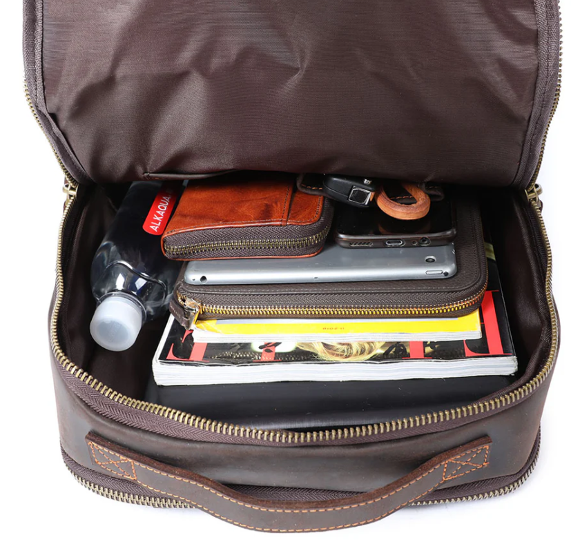 Interior view of the Loch Ness leather laptop rucksack, featuring notebooks, a water bottle, and organized accessories.