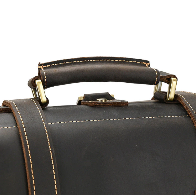 Close-up of a leather rucksack handle showing sturdy stitching and brass hardware for durability.