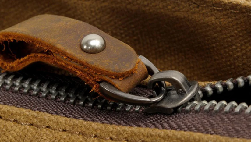 Close-up of a retro zipper on a shoulder bag, showcasing its vintage leather pull tab and sturdy metal teeth.