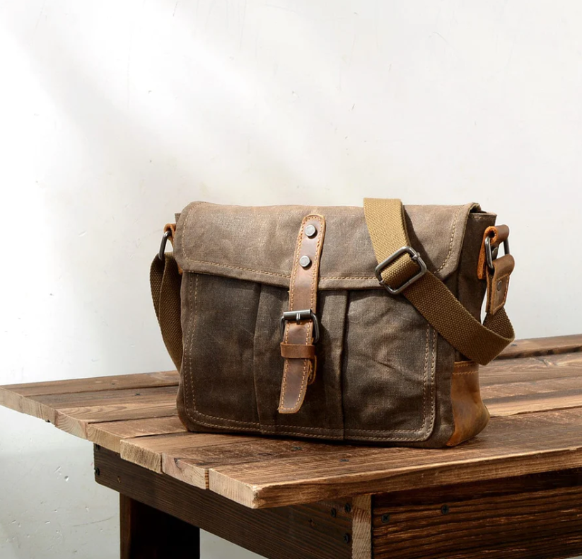 Small canvas messenger bag by Pyrenees, featuring a vintage design with leather accents, displayed on a wooden table.