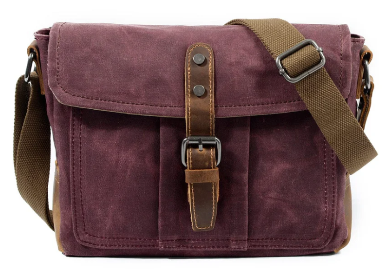 Small canvas messenger bag in deep purple with brown accents and adjustable shoulder strap, ideal for everyday use.