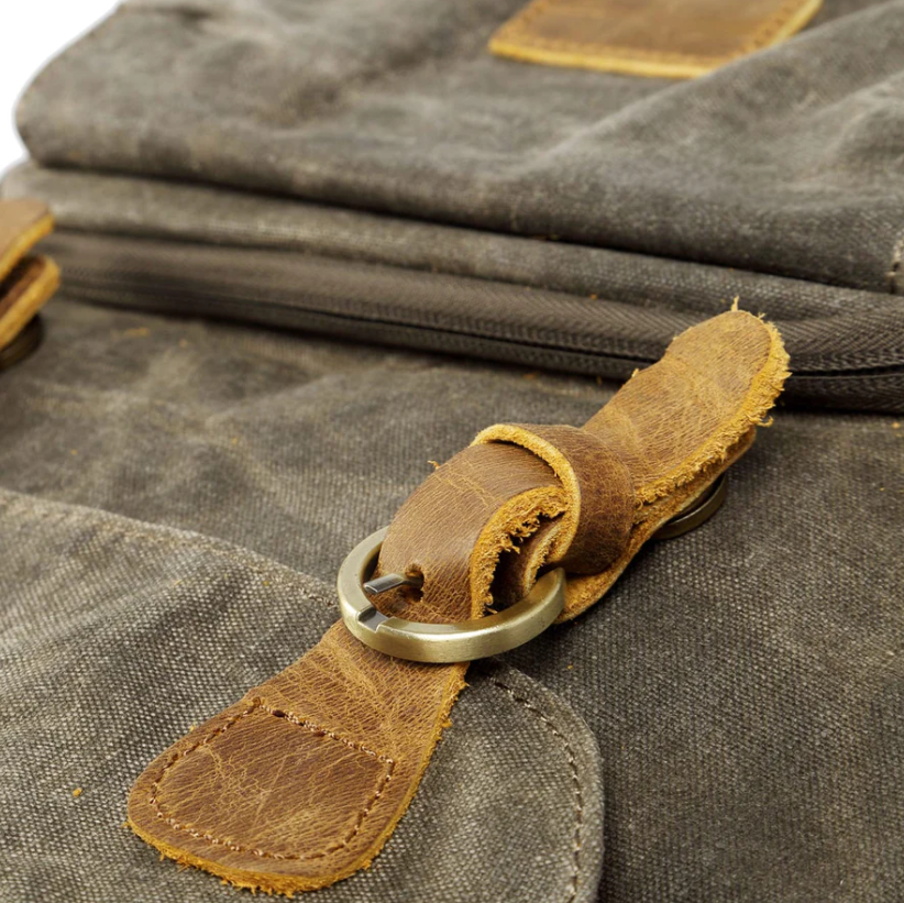 Close-up of the leather strap and brass buckle detail on a waterproof canvas camera backpack.