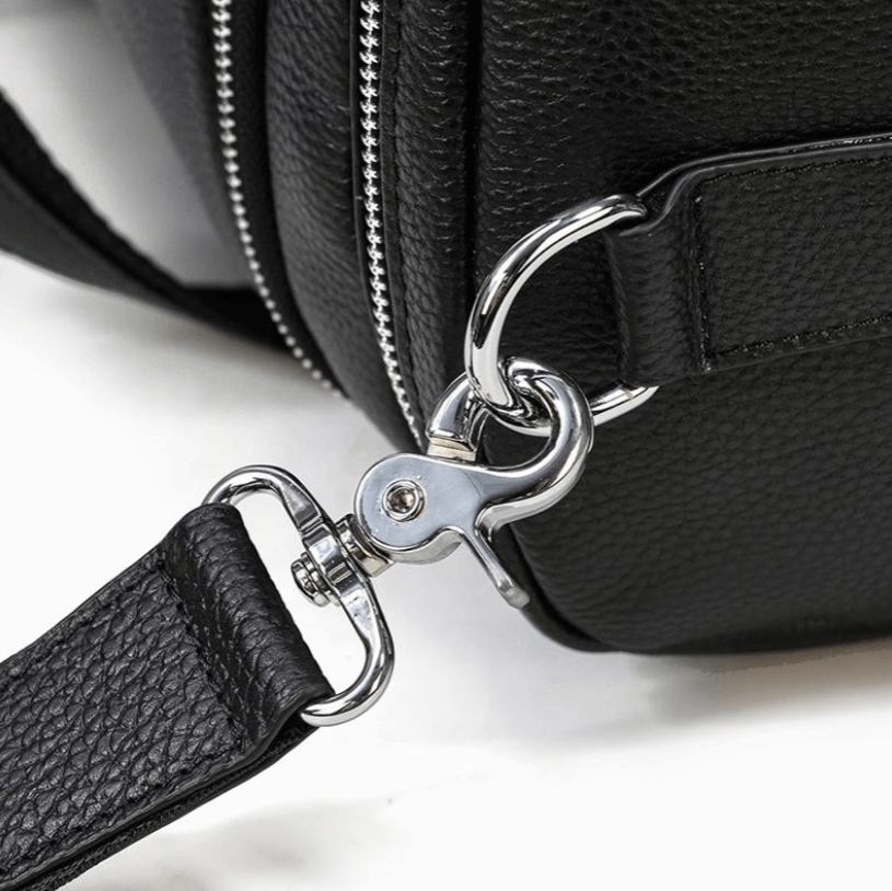 Close-up of the metal clip and strap of a black leather duffle bag, showcasing its stylish design and durability.