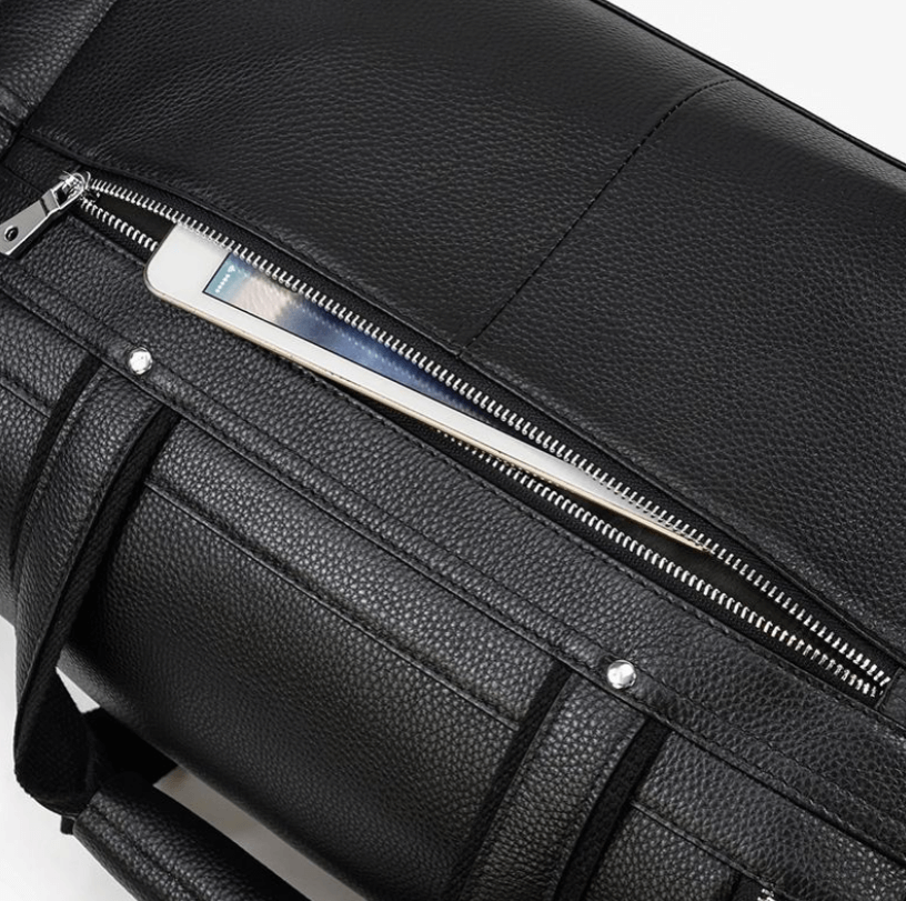 Close-up of a black leather duffle bag, featuring a zippered compartment with a smartphone partially visible.