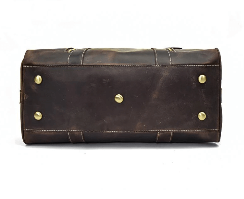 Bottom view of a brown leather overnight bag with brass studs, showcasing its sturdy craftsmanship and style.