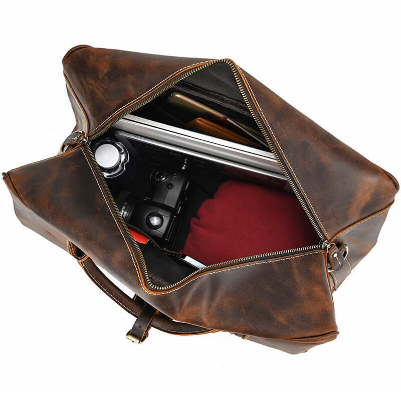 Inside view of a brown leather overnight bag showing camera, laptop, and clothing for travel.